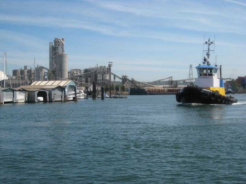 A boat navigates the Lower Duwamish River with industrial development on both sides of the river's banks. A boat navigates the Lower Duwamish River with industrial development on both sides of the river's banks.